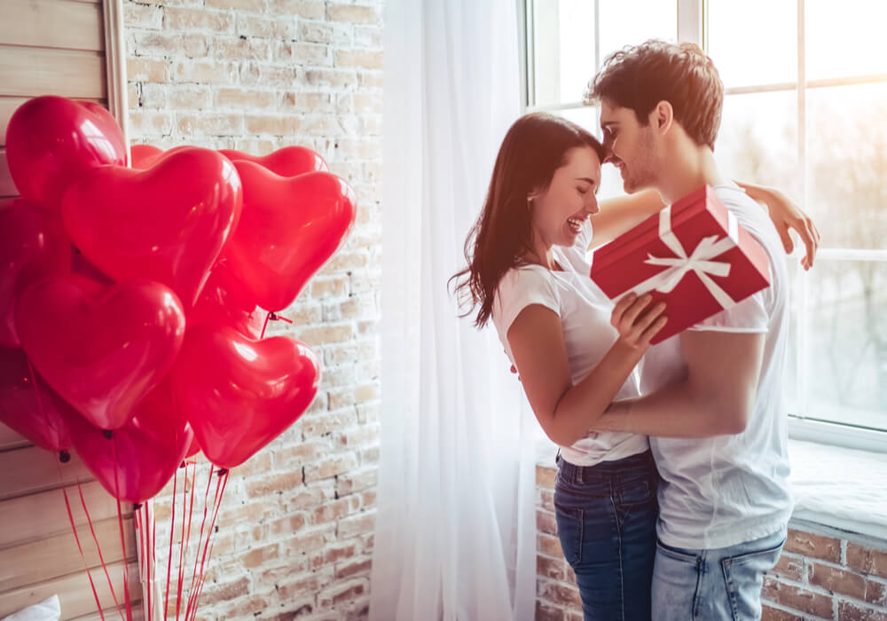 Young couple celebrating Valentine's Day with a gift and red heart balloons