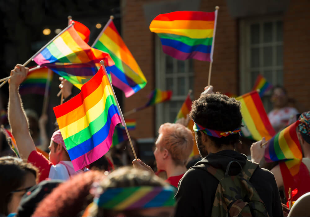 Large crowd celebrating Pride and waving rainbow flags