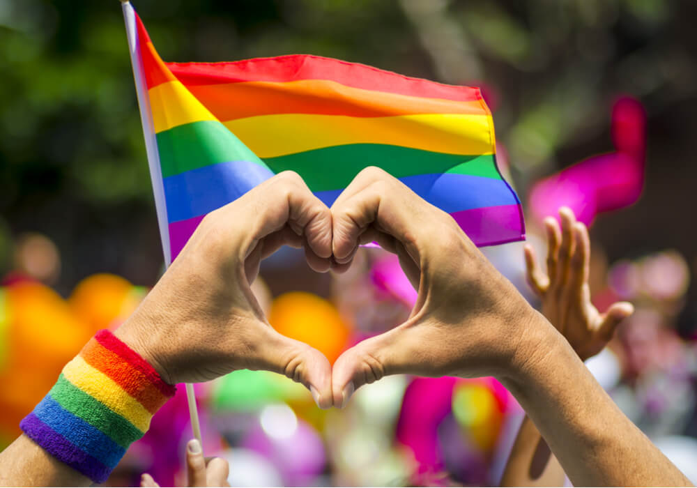 Hands making the shape of a heart with rainbow coloured flags for Pride