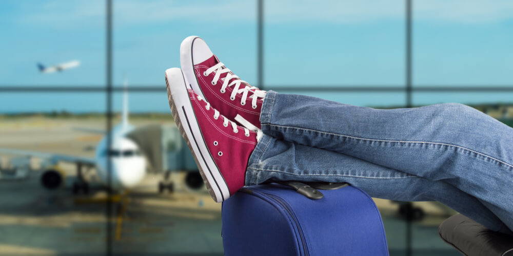 Man waiting for flight with feet up on suitcase and plane in the background